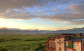 a house with a red roof sits on a grassy field near a road and mountains , under a cloudy sky at Newpark Resort