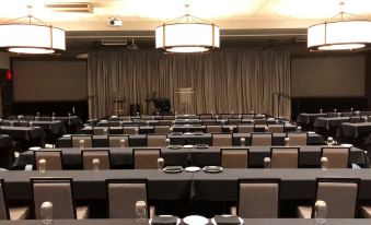 a large conference room with rows of tables and chairs , a chandelier hanging from the ceiling , and beige curtains covering the windows at Shangri-La Resort