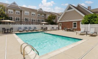 an outdoor swimming pool surrounded by a building , with lounge chairs and umbrellas placed around the pool area at Residence Inn Boston Foxborough