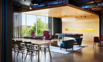 a modern living room with a pool table , purple chairs , and large windows overlooking trees at Aloft Leawood-Overland Park