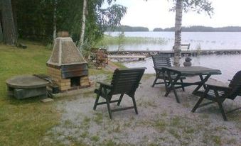 a wooden deck with picnic tables and chairs overlooks a lake , surrounded by trees and grass at Simola