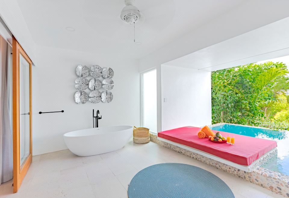 a modern bathroom with a white bathtub , a red bed , and a blue rug on the floor at Residences at Nonsuch Bay Antigua