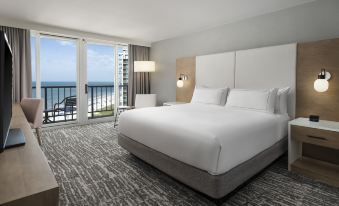 a large bed with white linens is in a room with a sliding glass door leading to an ocean view at Hilton Myrtle Beach Resort