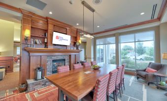 a large dining table with chairs is set up in front of a fireplace and television at Hilton Garden Inn Laramie