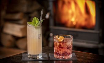 a glass of mixed drink and a glass with a strawberry garnish are on a table next to a fireplace at The Mill Hotel