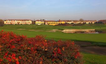 a golf course with a lush green field , surrounded by trees and buildings in the background at Doubletree by Hilton Milan Malpensa Solbiate Olona