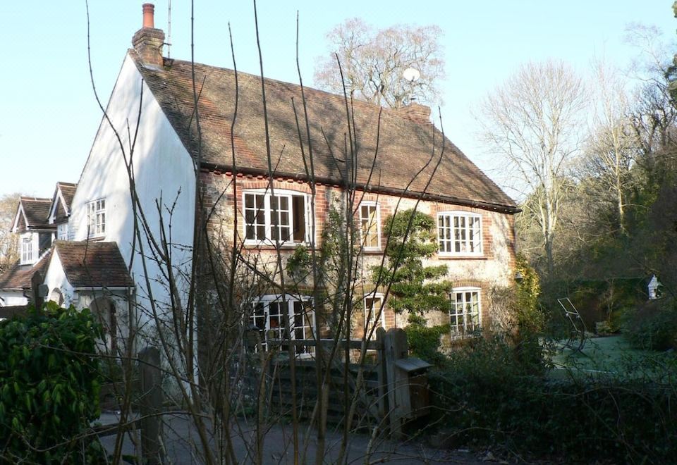 a white stone house with a red roof and brown trim , surrounded by trees and bushes at Bridge Cottage