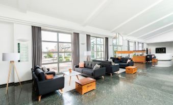 a modern living room with black leather couches , a wooden coffee table , and large windows at Hotel HerzogsPark