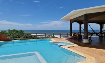 a large swimming pool with a patio and ocean view , under a covered area under a sunny sky at Hotel Miraflores