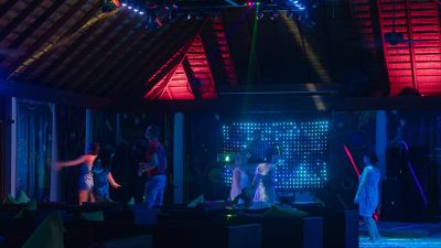 a stage with people performing on it , surrounded by neon lights and a wooden structure at Vilamendhoo Island Resort & Spa