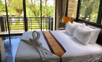 a well - arranged hotel bed with white linens and gold accents , set against a backdrop of lush greenery outside the window at Suwan Golf and Country Club