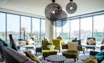 a modern living room with multiple chairs and couches arranged around a dining table , creating a cozy atmosphere at Hampton by Hilton Stockton on Tees