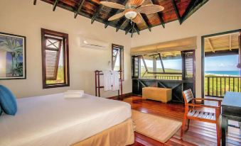 a bedroom with a bed , ceiling fan , and a bathroom with a bathtub overlooking the ocean at Santosha Barbados