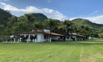 a large white building with a red roof is surrounded by palm trees and mountains at Las Jaras Aguas Termales