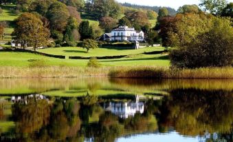 a large house is reflected in the water of a lake , surrounded by lush greenery at Ees Wyke Country House