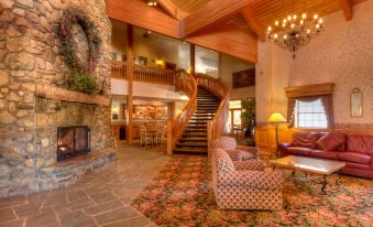 a spacious living room with a stone fireplace , wooden stairs , and a large chandelier hanging from the ceiling at The Inn at Holiday Valley