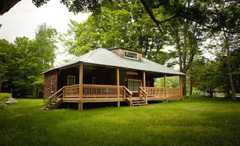 a large wooden cabin with a green roof and wooden porch is surrounded by green grass and trees at Blue Hill Lodge