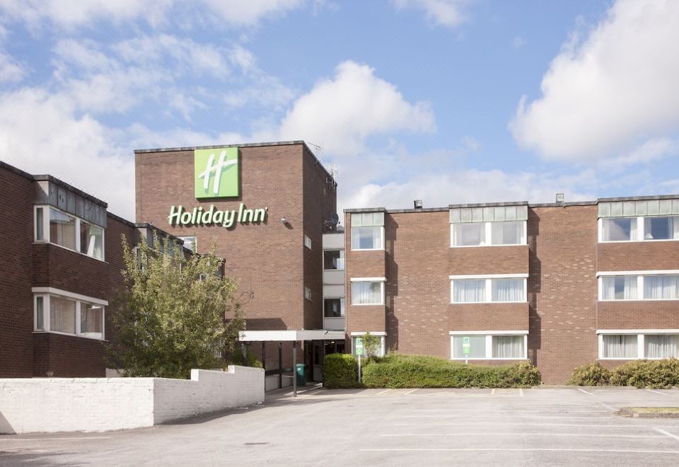 a large brick building with a hotel sign on the side and a parking lot at Holiday Inn Leeds - Wakefield M1, Jct.40