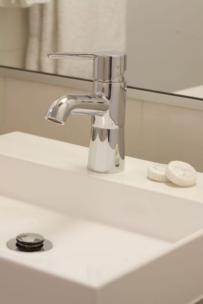 a modern bathroom sink with a chrome faucet , white soap dispenser , and round soap holders at Ibis Melbourne Hotel and Apartments