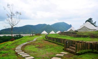 a grassy field with a wooden walkway leading to several white tents , possibly for camping or glamping at Chiangkhan River Green Hill