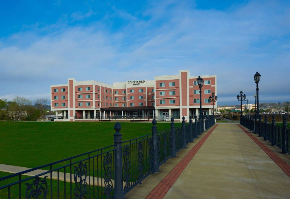 a large , red - brick hotel building with a green lawn in front of it , under a clear blue sky at Courtyard Rome Riverwalk