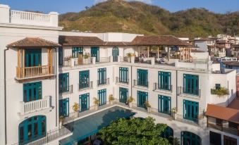 a large , white building with blue shutters and a balcony is surrounded by greenery and has people sitting on the balcony at Santarena Hotel at Las Catalinas