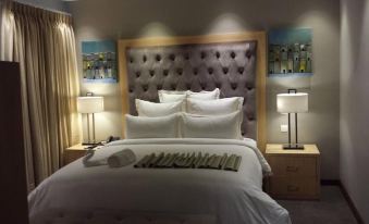 a large bed with white linens and a tufted headboard is shown in a hotel room at Grand Palace Hotel Mzuzu