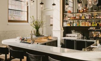 a modern bar with a curved counter , black chairs , and various bottles and glasses on shelves at August