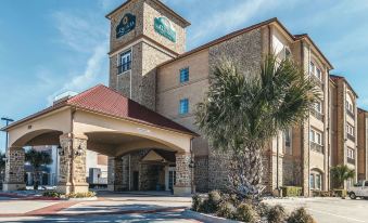 a large , stone building with a red roof and a palm tree in front of it at La Quinta Inn & Suites by Wyndham Dallas Grand Prairie South