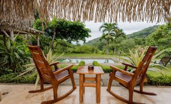 a wooden rocking chair with a table and pillows is situated in front of a pool at Punta Islita, Autograph Collection