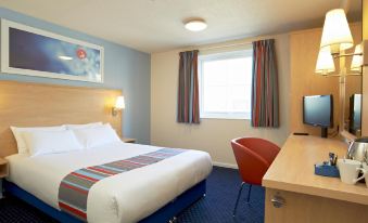 a large bed with a blue and white striped blanket is in the center of a hotel room at Travelodge Stafford M6