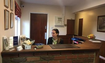 a woman is sitting at a reception desk in a hotel lobby , waiting to assist guests at The Cedars Hotel