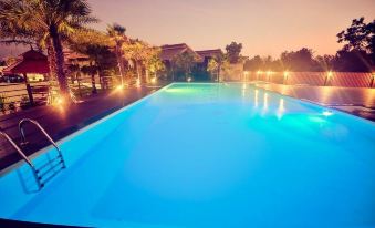 a large , rectangular swimming pool with blue water illuminated by lights at night , surrounded by palm trees and a building in the background at Chanalai Resort and Hotel