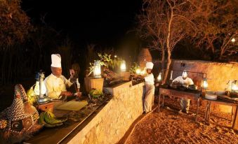 a group of chefs preparing food on a stone grill in an outdoor setting at night at Elewana Tarangire Treetops