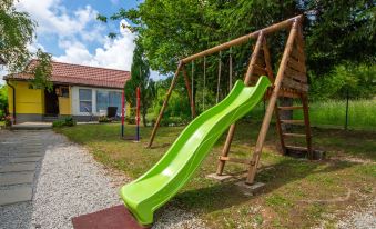 a wooden playground with a green slide , swings , and other play equipment in a grassy area near a house at Tina