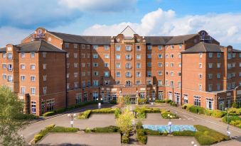 a large brick building with a swimming pool in the courtyard , surrounded by trees and bushes at Doubletree by Hilton Dartford Bridge