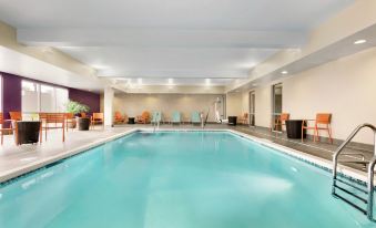 a large , empty swimming pool with blue water and white tiles , surrounded by lounge chairs and a wooden ceiling at Home2 Suites by Hilton Middletown