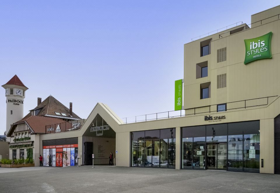 a modern building with a green sign and two skyscrapers , situated in a bustling city street at Ibis Styles Paris Romainville