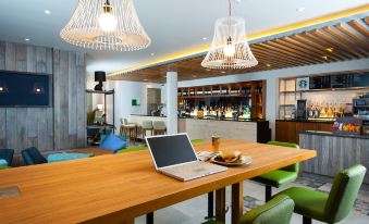 a wooden dining table with a laptop placed on it , surrounded by chairs and a bar at Holiday Inn Salisbury - Stonehenge