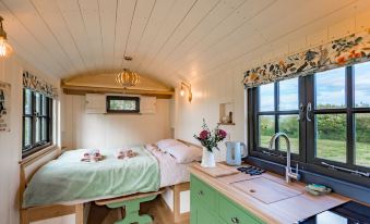 a cozy bedroom with a bed , kitchenette , and window , decorated in white and green colors at Corner House