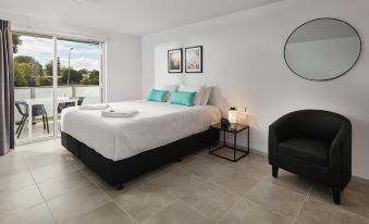 a modern bedroom with a white bed , black nightstand , and black chair , along with a small table and a mirror at East Maitland Executive Apartments