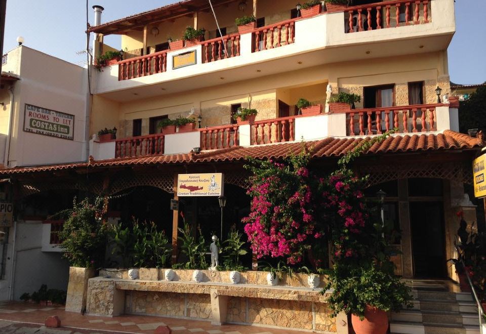 a building with a balcony , surrounded by plants and flowers , and a small fountain in front of it at Costas Inn