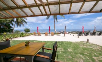 a wooden patio overlooking the ocean , with a dining table and chairs set up for a meal at Reef Beach Resort