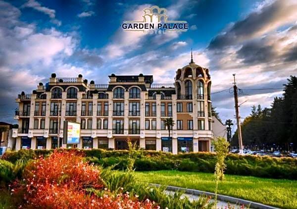 a large building with a tall tower and balcony is surrounded by greenery and red flowers at Garden Palace