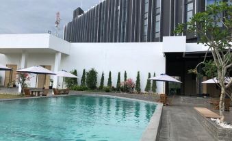 a large swimming pool is surrounded by white lounge chairs and umbrellas , with a building in the background at BBC Hotel Lampung Bandar Jaya