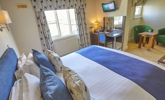 a large bed with blue and white bedding is in a room with a desk , chair , and television at The Cadogan Arms