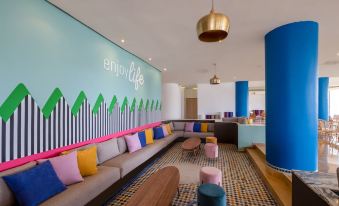 "a colorful living room with a blue couch , wooden stools , and a wall mural that says "" enjoy life "" on it" at Allegro Agadir