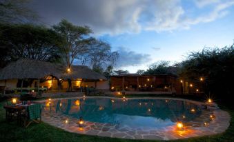 a serene outdoor setting with a pool , surrounded by trees and lit up by lanterns at dusk at Elewana Lewa Safari Camp