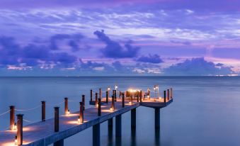 a wooden pier extending into the ocean at sunset , illuminated by lanterns and surrounded by calm water at Four Seasons Resort Seychelles at Desroches Island