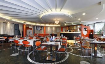 a modern restaurant with orange chairs and tables , a white ceiling fan , and black and white checkered flooring at Hotel Pineta